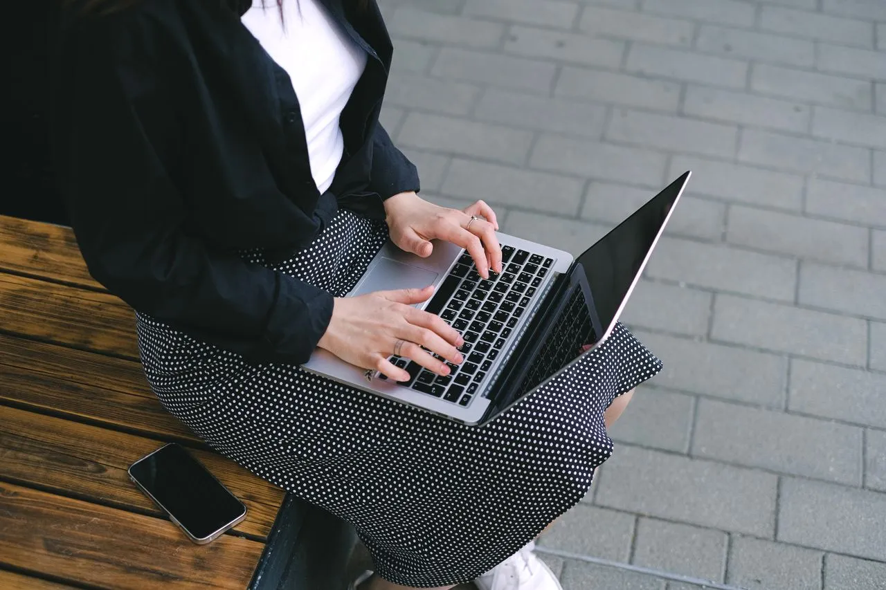 Woman sitting outdoors typing on a laptop, embodying freelance and digital nomad lifestyle.