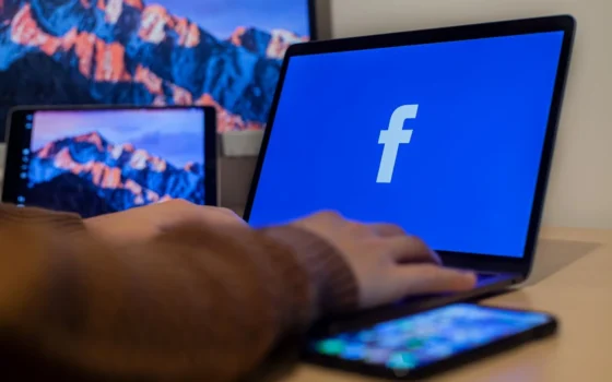 Laptop displaying Facebook at workspace with multiple devices, highlighting modern technology.