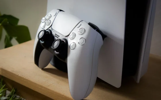 Close-up of PlayStation 5 with DualSense controller on a wooden shelf.